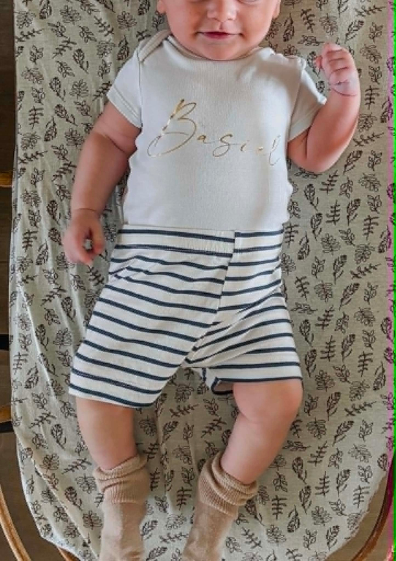 Baby in wit rompertje met de naam Basiel in goudkleurige letters