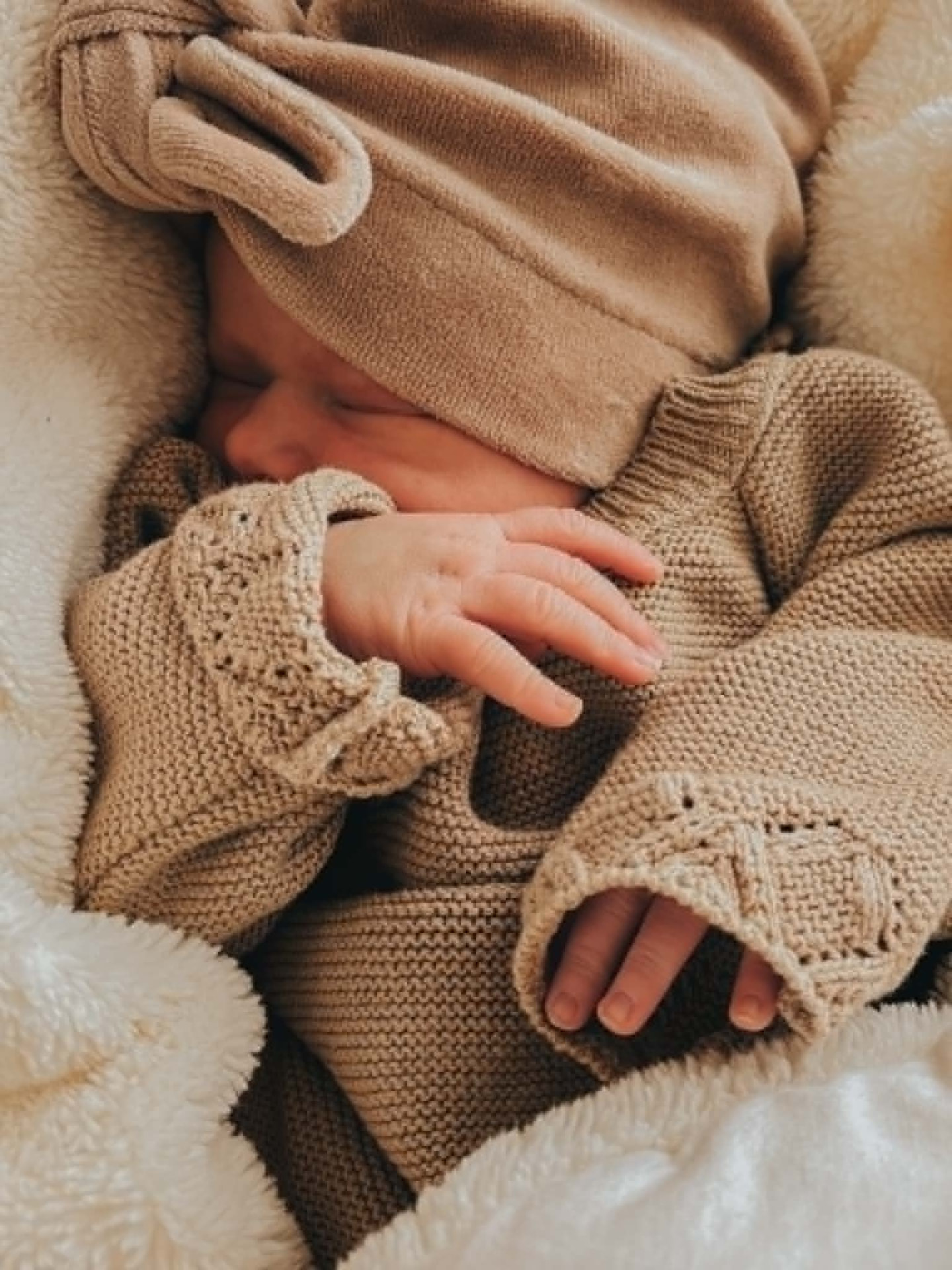 Newborn in beige gebreide kleding met kleine handjes